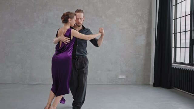 Camera slowly moving to a pair sensually dancing a tango in a grey studio. Full growth shot of people dancing. Slow motion dancing tango. High quality 4k footage