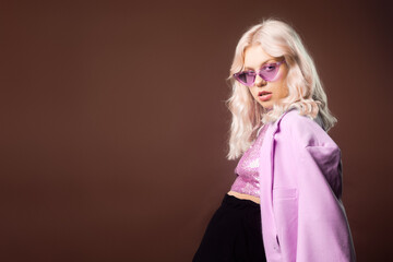 Blonde in a pink jacket with glasses, a jacket with sequins posing in the studio on a brown...