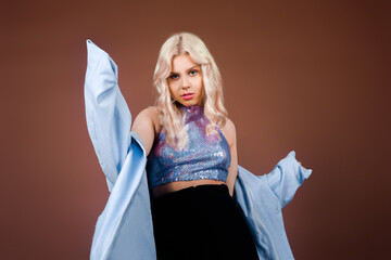 A blonde in a turquoise jacket, in a blue jacket in sequins, poses in the studio on a brown...