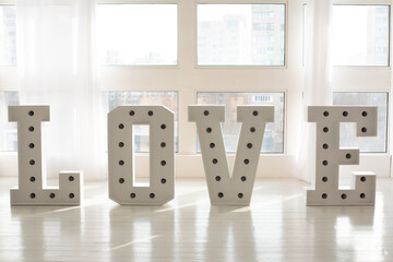 Love big white letters with led retro bulbs glowing. Word LOVE with a big letters. Inscription is love. Glowing large letters. Wedding decor. Illuminated Love sign in large letters near window. 