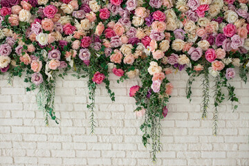 Beautiful decorative colorful roses and peonies on brick white wall. Interior wedding party decor. Wall with curly Flowers. Brick wall with beautiful flowers in room. Summer flowers on wall building. 
