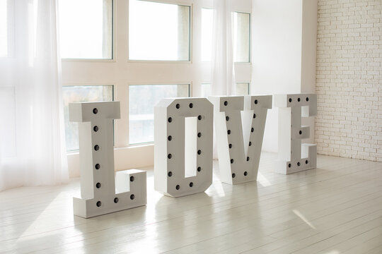 Word LOVE with a large letters. Inscription is love. Wedding decor. Illuminated Love sign in big letters near window. Love big white letters with led retro bulbs glowing. valentine's day, february 14