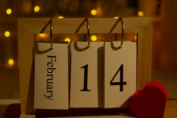 Wooden calendar with the date February 14 on the background of the festive bokeh. The concept of a...