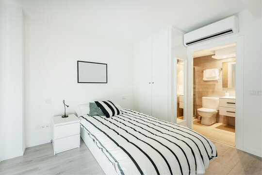 Bedroom with white walls and furniture with small bed, air conditioner and individual bathroom