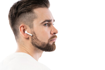 Obraz premium Handsome bearded man in white clothes using wireless earbuds on white background