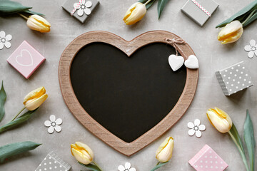 Yellow tulips, deco flowers and gift boxes. Springtime background with copy-space on heart shaped letter board, letterboard. Spring flat lay on light grey stone background.