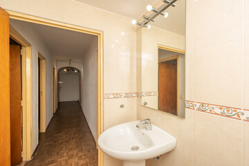 Bathroom with a white porcelain sink below a frameless mirror on the side of a hallway
