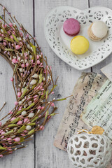 Moscow, Russia, January 2022 multi-colored macaroons in a plate in the form of a heart on a table made of white boards with noiami and a wreath of spring branches