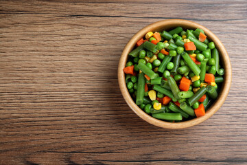 Mix of fresh vegetables in bowl on wooden table, top view. Space for text
