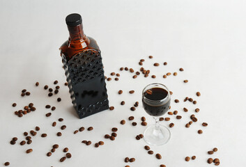 Coffee liqueur in dark glass bottle and poured into a glass. White background, scattered coffee beans