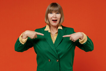 Elderly exultant amazed surprised caucasian woman 50s in green classic suit point index fingers on herself isolated on plain orange color background studio portrait. People business lifestyle concept.