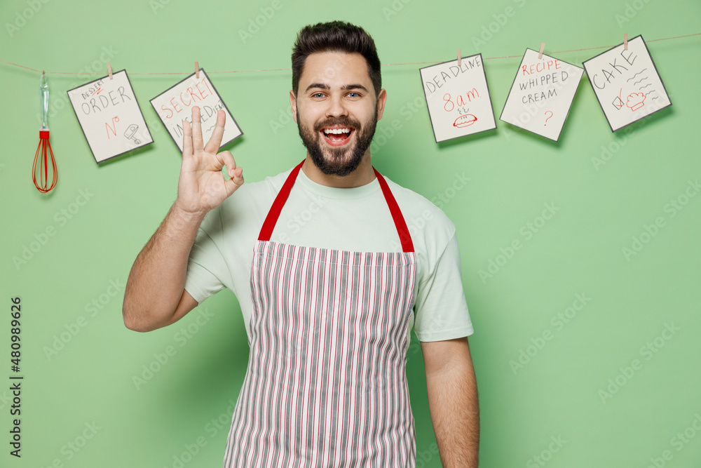 Sticker Young satisfied cheerful cool male chef confectioner baker man 20s wearing striped apron showing okay ok gesture isolated on plain pastel light green background studio portrait. Cooking food concept.