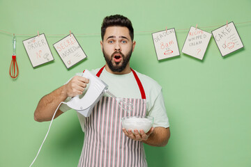 Young amazed male chef confectioner baker man 20s in striped apron using mixer whisk eggs for cake dessert cooking isolated on plain pastel light green background studio portrait Cooking food concept
