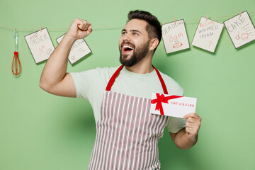 Young chef confectioner baker man in striped apron hold gift certificate coupon voucher card for...