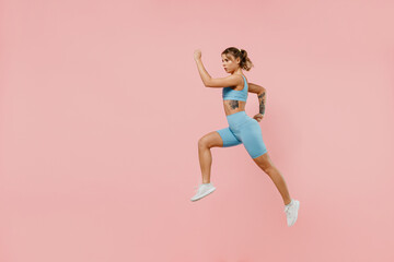 Fototapeta na wymiar Full body young strong sporty athletic fitness trainer instructor woman wear blue tracksuit spend time in home gym jump high run isolated on pastel plain light pink background. Workout sport concept.