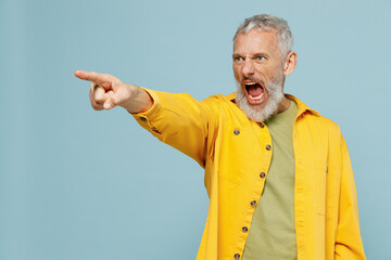 Elderly angry strict indignant gray-haired mustache bearded man 50s wear yellow shirt point index finger aside scream isolated on plain pastel light blue background studio. People lifestyle concept.