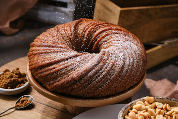 Tasty Muffin cake or Bundt cake sprinkling icing sugar on the stand. Sieving powdered sugar on a...
