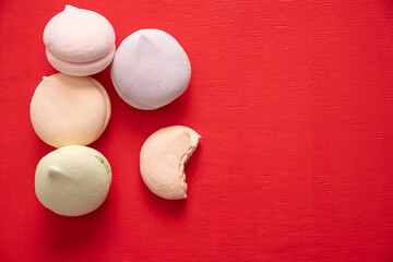 Round multi-colored marshmallows in a pile and one bitten half of a marshmallow on a red background