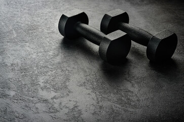 A pair of black dumbbells on a dark concrete background with copy space. The concept of hard training.