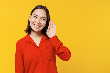 Curious nosy stunning charming vivid fun young woman of Asian ethnicity 20s years old wear orange shirt try to hear you overhear listening intently isolated on plain yellow background studio portrait