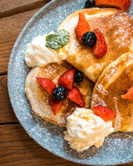 Fresh pancakes with strawberries, blueberries, whipped cream and maple syrup. Scrambled eggs and bread in the background. Brunch in a coffee shop.