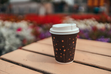 Paper coffee cup on wooden table in outdoor cafe.
