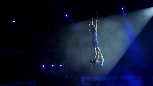 Aerial acrobat on the circus stage. A young girl and a guy perform acrobatic elements on the air ring, in the circus arena. Circus artists create shows for the audience. Flexible, athletic, aerialists
