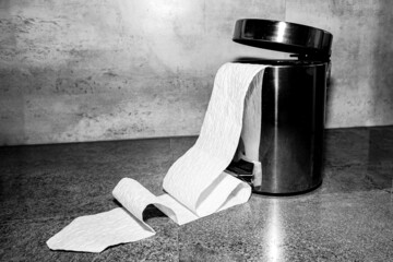 Fotografía conceptual de una papelera tragándose un rollo de papel higiénico, en blanco y negro.