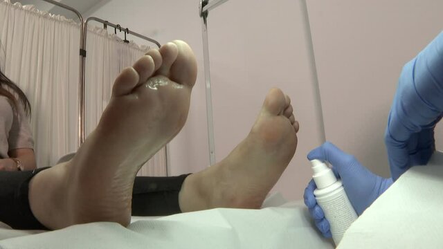 Close up of beautician hands in sterile gloves spraying lotion on lady feet before the procedure