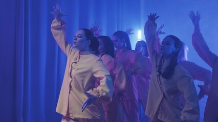 A group of beautiful girls dancing in a room with blue lighting in yellow suits. Dances