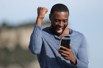 Man with black skin celebrating checking phone - obrazy, fototapety, plakaty