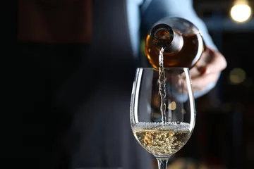 Rolgordijnen Bartender pouring white wine from bottle into glass indoors, closeup. Space for text © New Africa