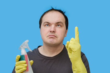 A janitor with an idea raised his index finger up in yellow gloves , a portrait on a studio blue background