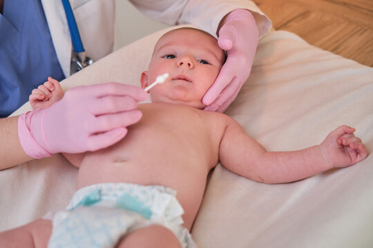 The Doctor Performs The Hygiene Of The Nose And Ears Of The Newborn Baby With A Cotton Swab. Nurse In Uniform Rubs The Skin Of A Child