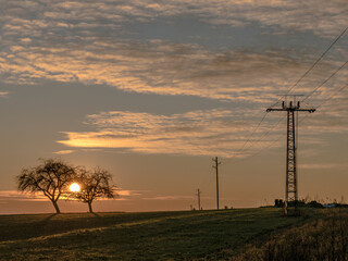 Obraz premium Strommast und Feldweg bei Sonnenuntergang
