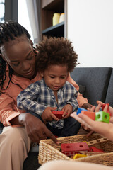 Family playing with little son at home, sitting on sofa and taking toys ot of basket