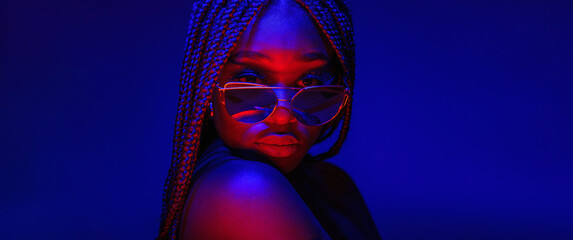 Portrait of fashion young girl in sunglasses in red and blue neon light in the studio