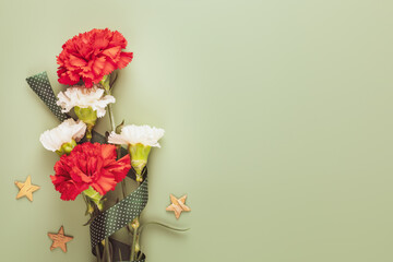 Mans Day holiday card with red and white carnations with gift ribbon and wooden stars on a green...