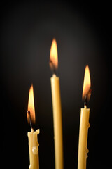 Three burning thin wax candles on a dark background