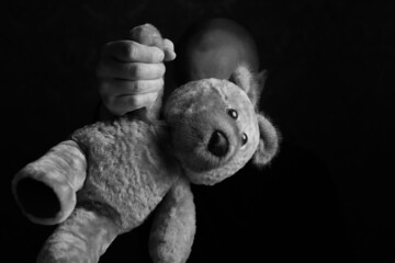 A man's hand holds a teddy bear by the paw, the focus is in the foreground. Conceptual photo: rude...