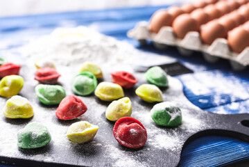 colored dumplings on a bright blue wooden background, on a black board, flour is scattered next to a package of raw eggs