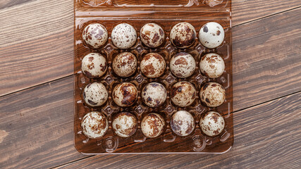 Group of quail eggs are put on clear tray on wooden table.