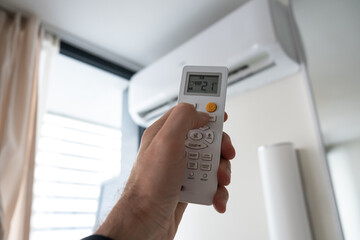 A man's hand holds a remote control from an air conditioner with a temperature on the screen of 21.