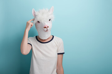 Young woman in alpaca mask point index finger to the head, isolated on blue background.