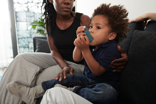 Worried mother looking at little son holding inhaler to treat asthmatic attack