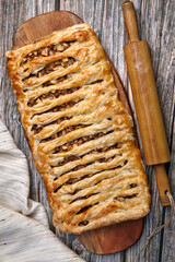 A wicker apple strudel pie with walnuts lies on a cutting board