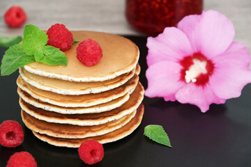 Pancakes with fresh raspberries, mint and jam on a black table with lonicera