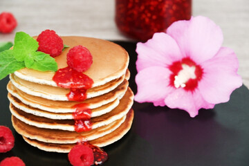 Pancakes with fresh raspberries, mint and jam on a black table with lonicera