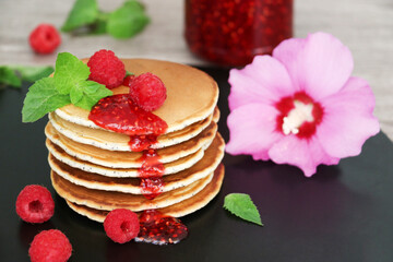 Pancakes with fresh raspberries, mint and jam on a black table with lonicera