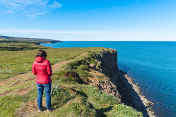 Woman hiker admiring a rugged coast from a clifftop path in Iceland on a sunny summer day